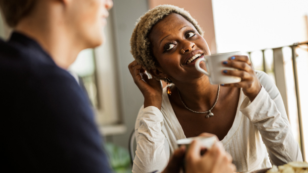 En kvinna dricker en kopp kaffe medan hon pratar med en man.